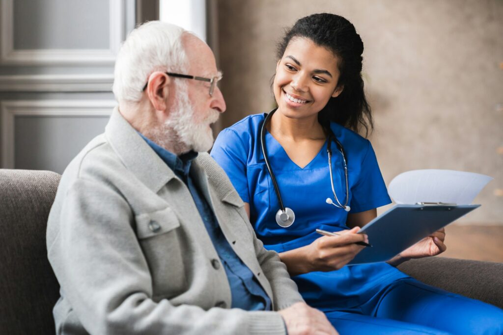 Happy young skilled female general practitioner in blue medic uniform visiting disabled